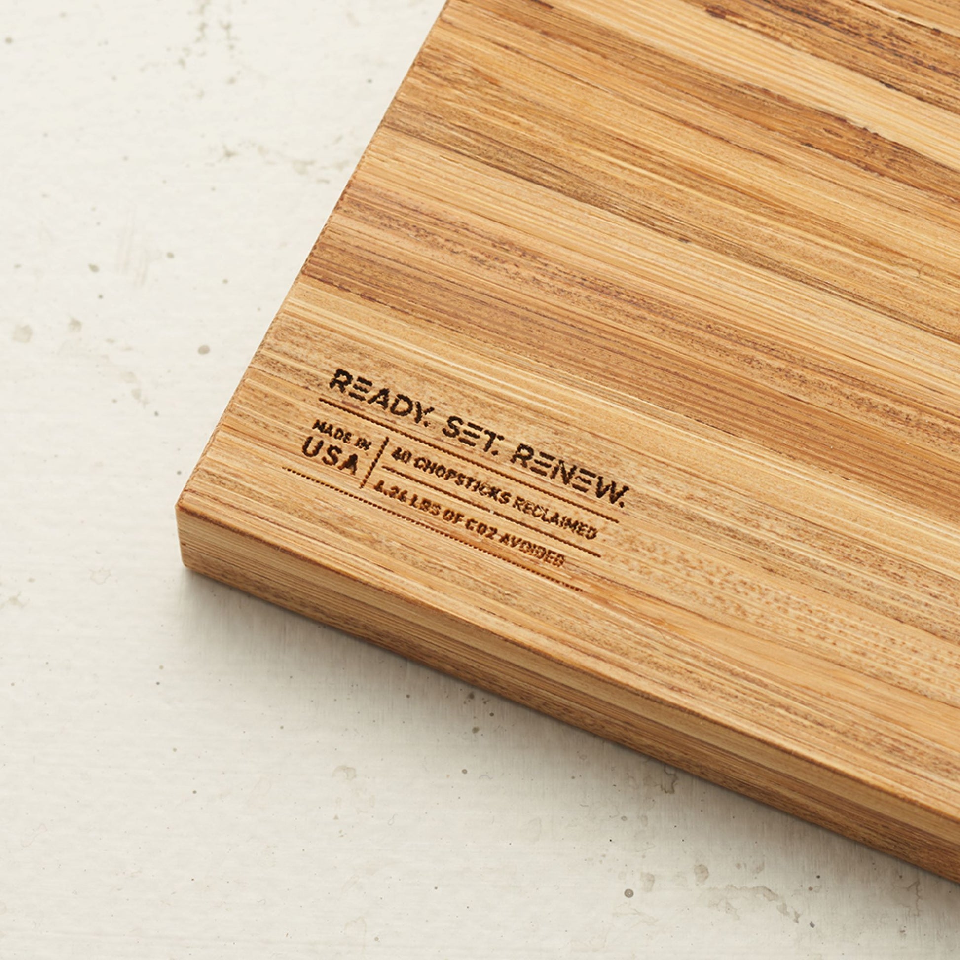 Close up view of the stamp on the back of the board that reads renew made in the usa forty chopsticks reclaimed and four point two four pounds of co2 avoided