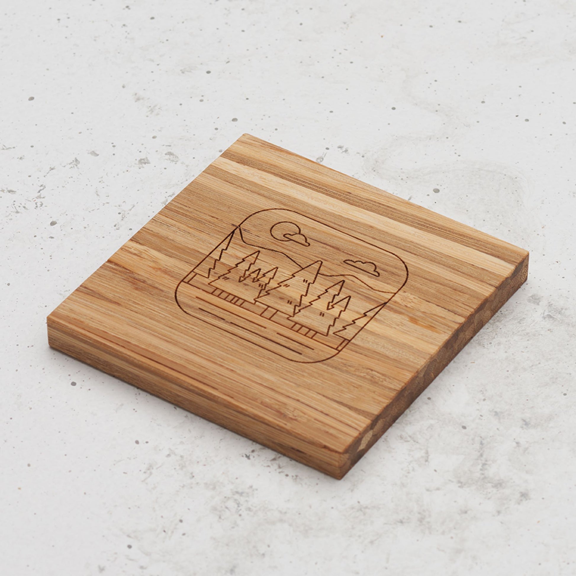 An overhead view of one of the all day every day coasters with an engraved image of a forest in the middle