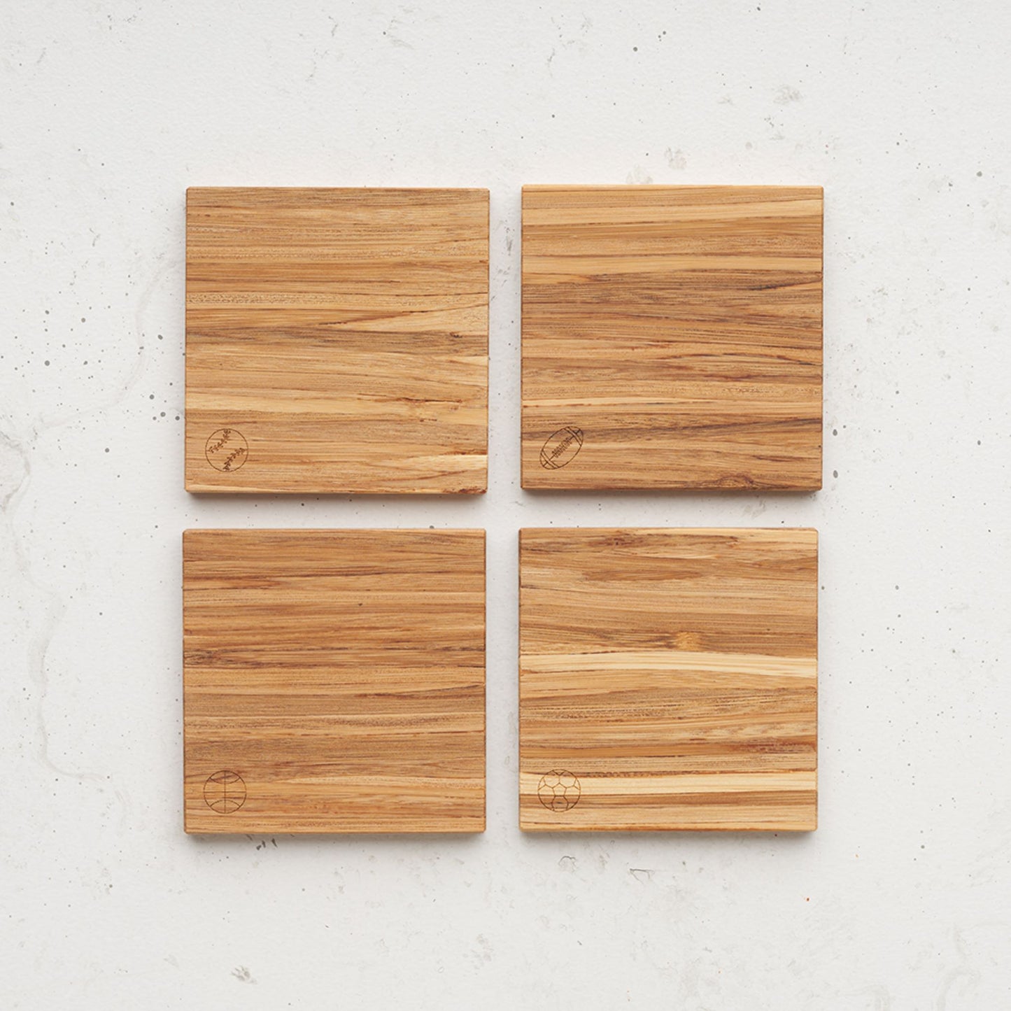 An overhead view of the game time themed all day every day coasted set. Each coaster has a different game time ball etched in the bottom left corner. There is a basketball, football, soccer ball and also a baseball.