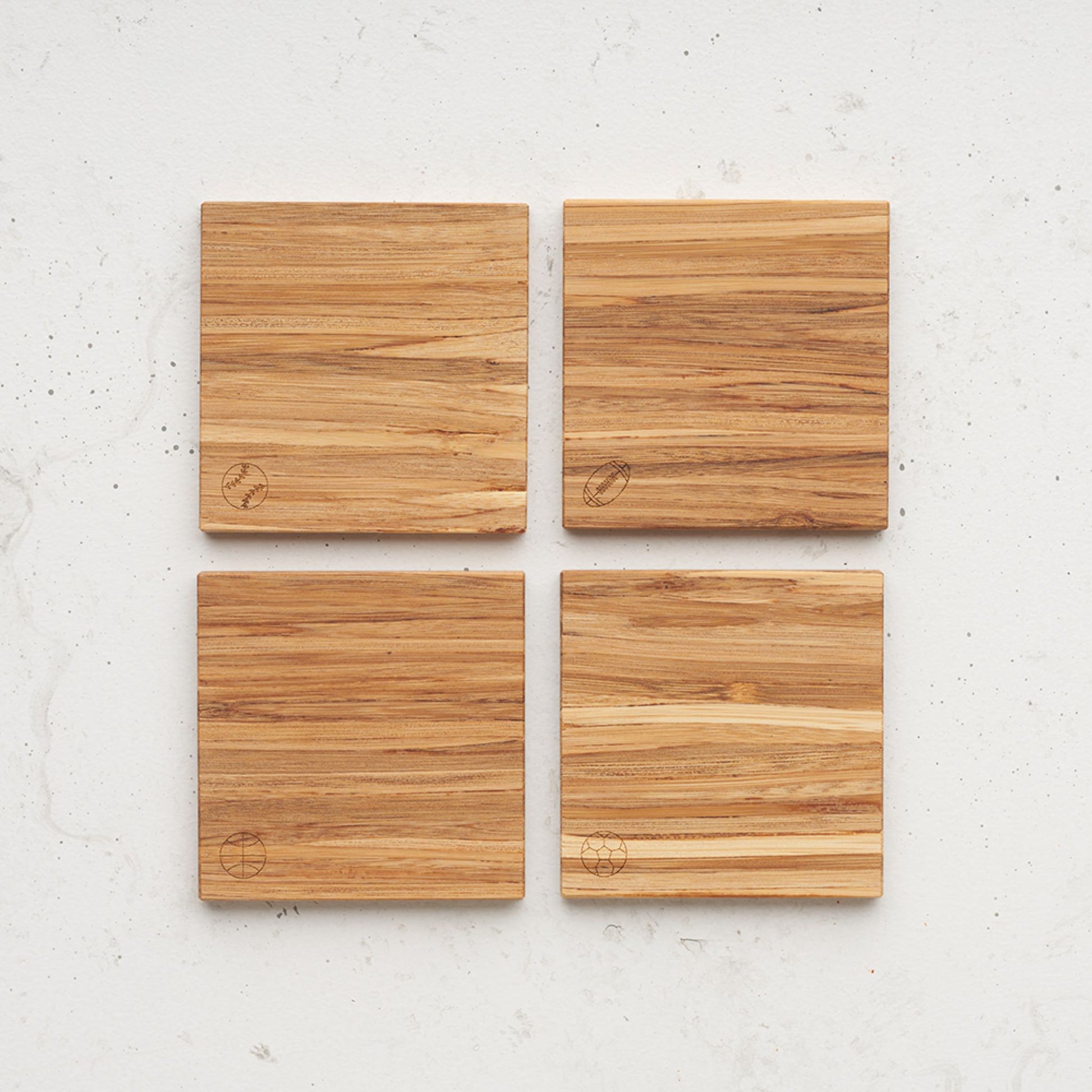 An overhead view of the game time themed all day every day coasted set. Each coaster has a different game time ball etched in the bottom left corner. There is a basketball, football, soccer ball and also a baseball.