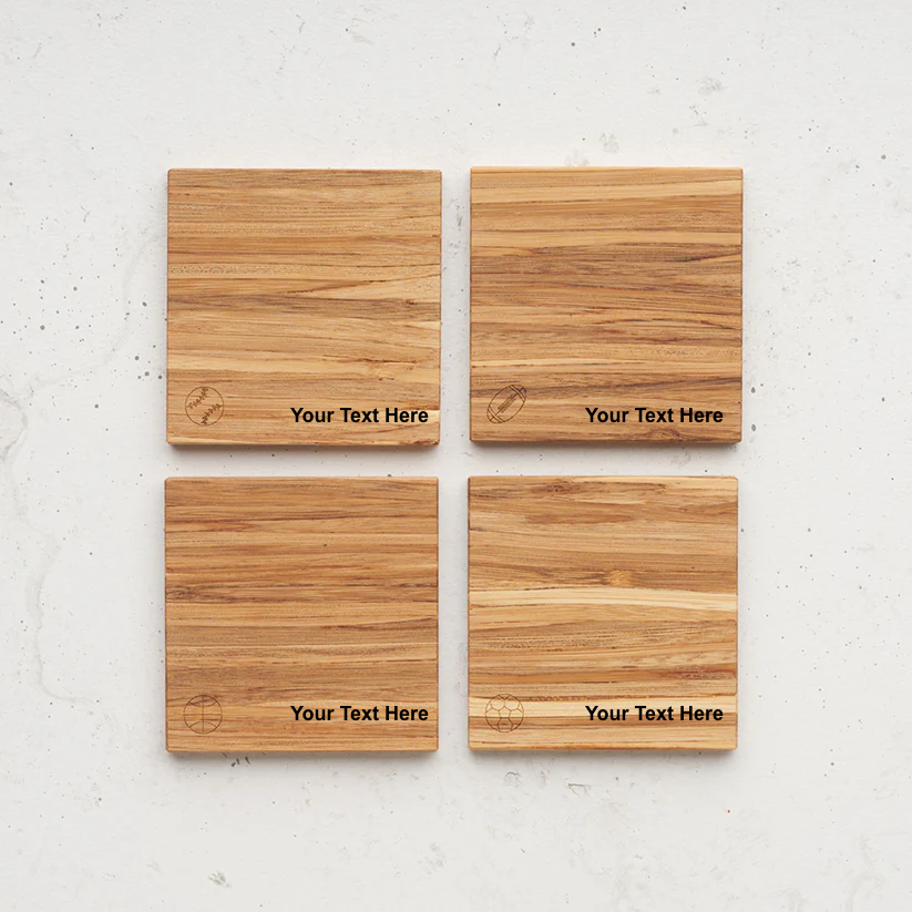 An overhead view of the backside of the entire game time themed all day every day coaster set sitting on a counter. Each coaster features an engraved sports icon in the bottom left and the placeholder text "Your Text Here" engraved to its right: baseball, football, basketball, and soccer ball.