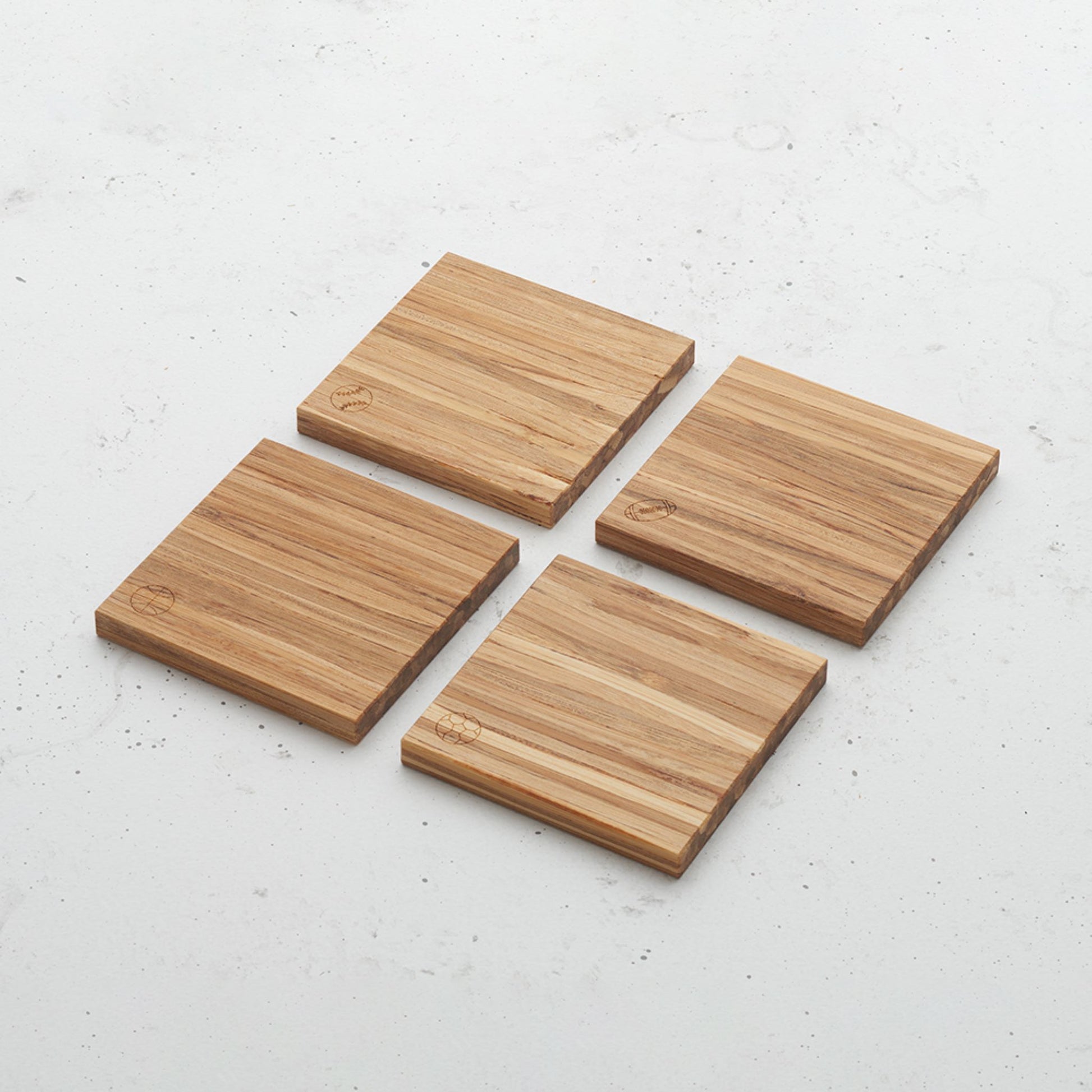 An overhead view of the game time themed all day every day coaster set. Each coaster has a different game time ball etched in the bottom left corner. There is a basketball, football, soccer ball and also a baseball.