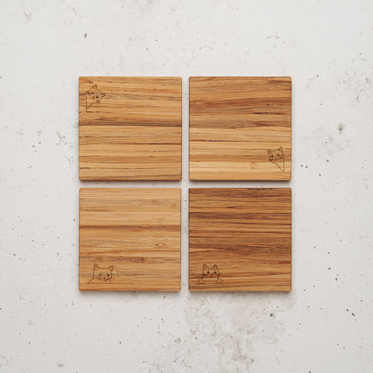 An overhead view of the entire 9 lives cat themed all day every day coaster set sitting on a counter top with the image of a cat's head engraved in each of the corners