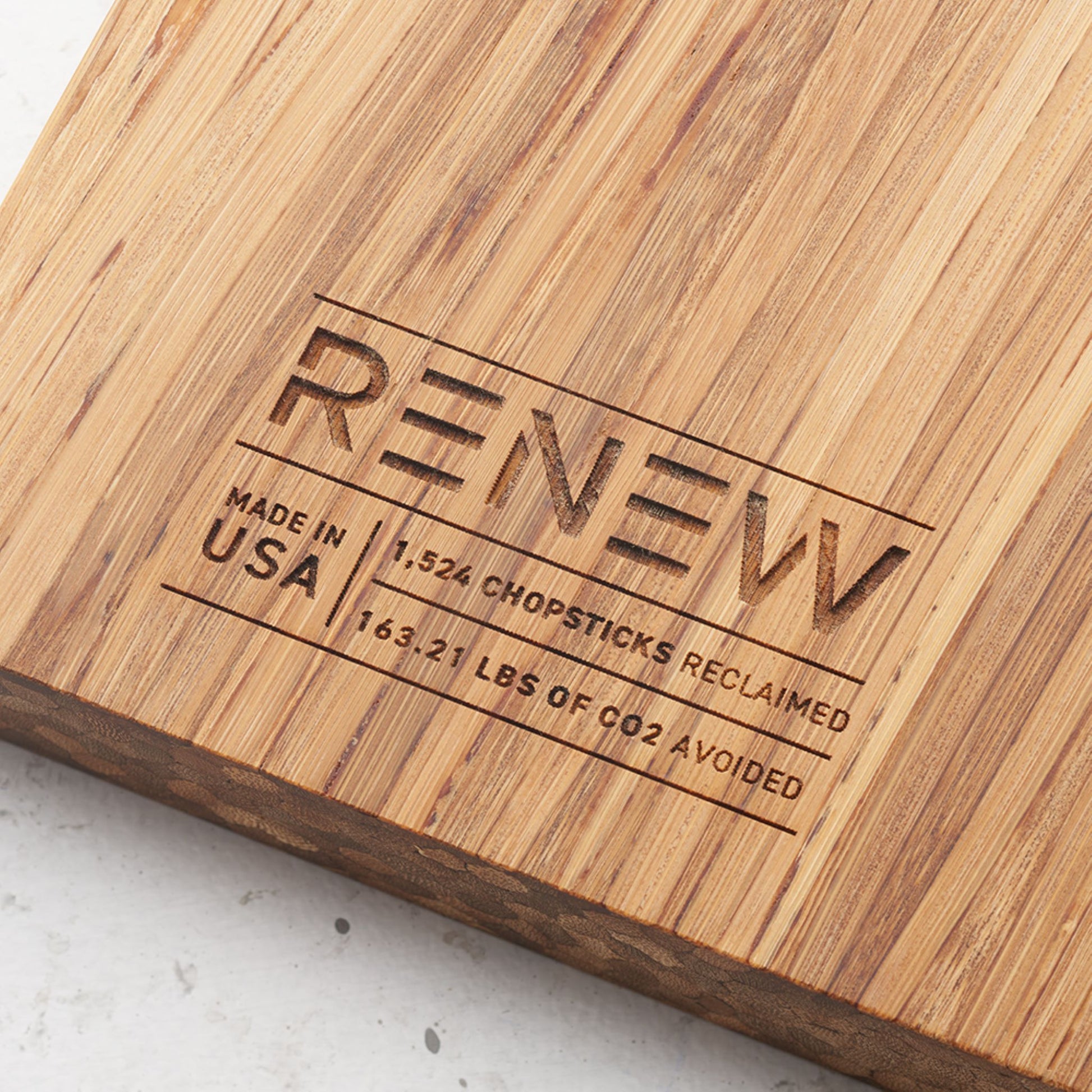 Close up view of the stamp on the back of the board that reads renew made in the usa one thousand five hundred and twenty four chopsticks reclaimed and one hundred and sixty three point twenty one pounds of co2 avoided