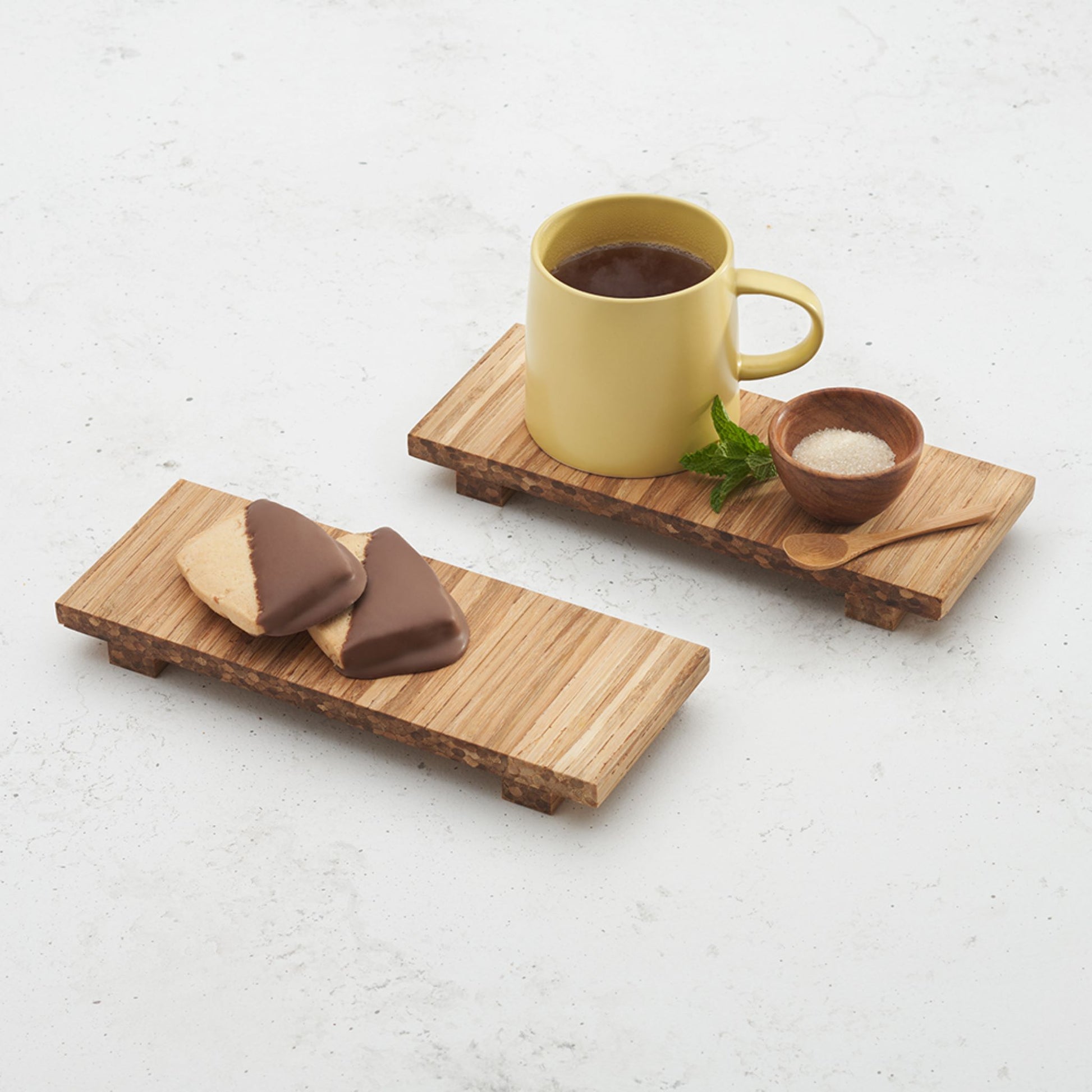 two heyday breakfast trays sitting on the countertop, one with a coffee mug, a small bowl of sugar, and a mini spoon on top, another with two biscuits on top