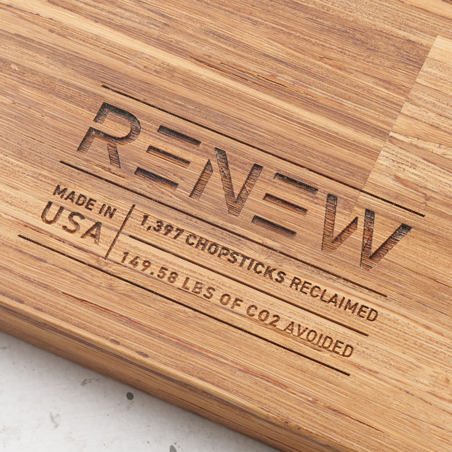 Close up view of the stamp on the back of the board that reads renew made in the usa one thousand three hundred and ninety seven chopsticks reclaimed and one hundred and forty nine point five eight pounds of co2 avoided