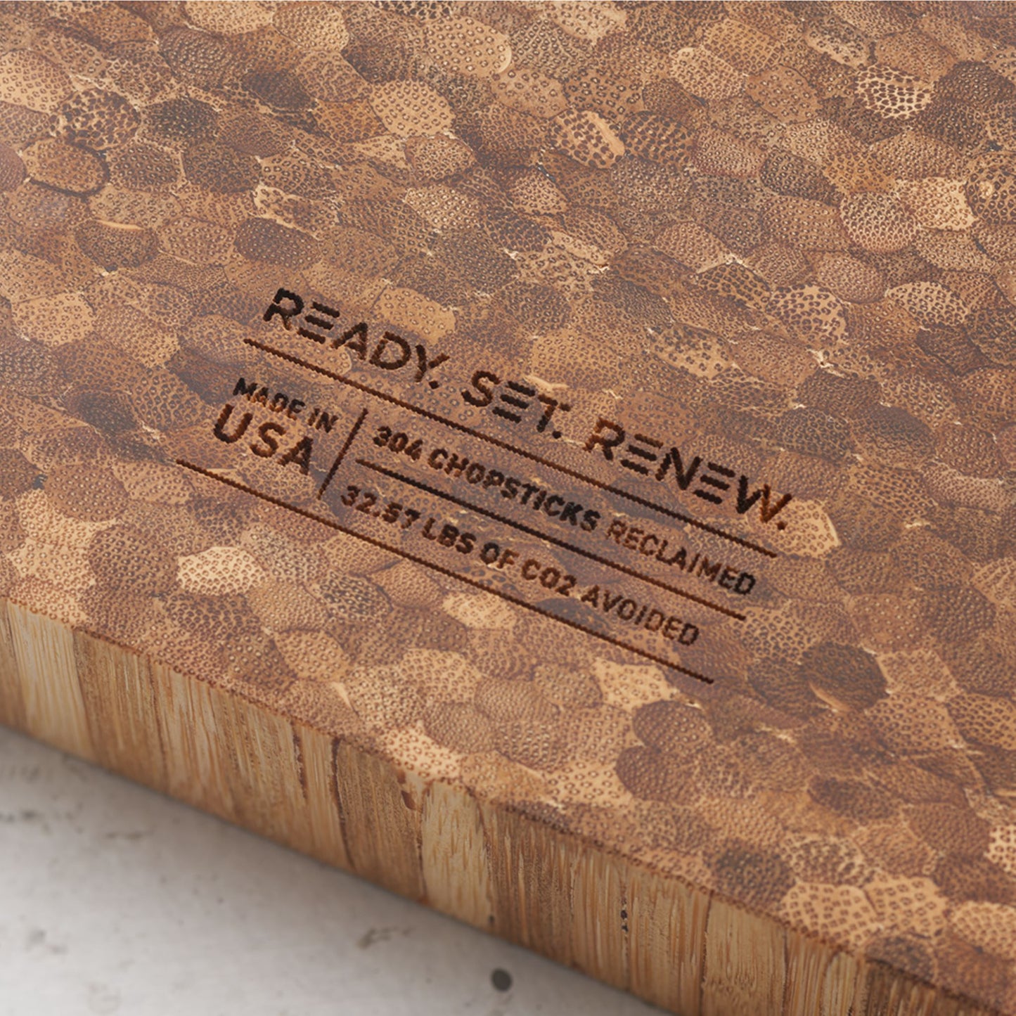 Close up view of the stamp on the back of the board that reads renew made in the usa three hundred and four chopsticks reclaimed and thirty two point five seven pounds of co2 avoided