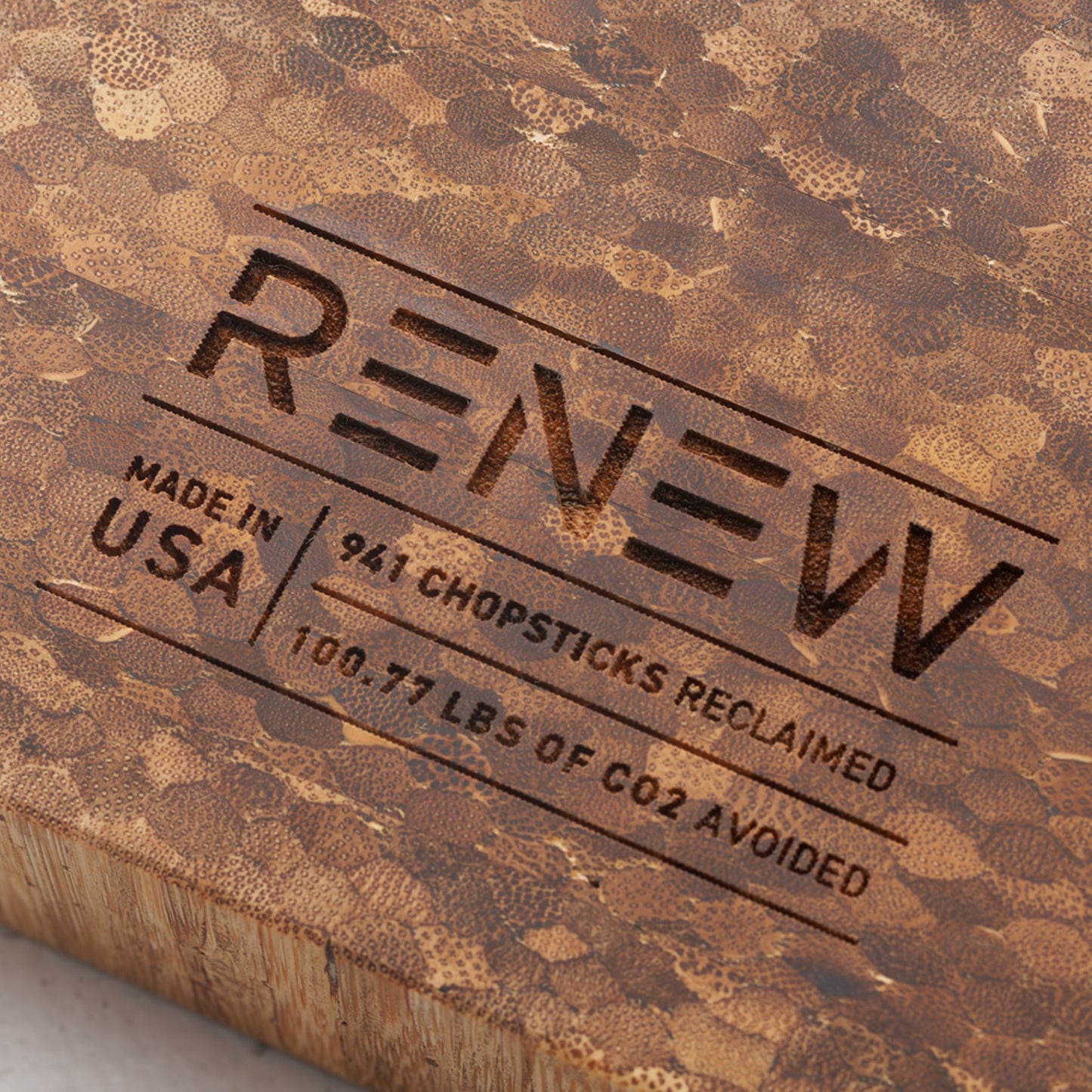 Close up view of the stamp on the back of the board that reads renew made in the usa nine hundred and forty one chopsticks reclaimed and one hundred point seventy seven pounds of co2 avoided