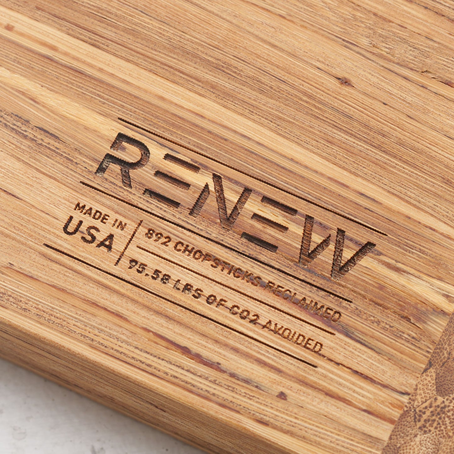 Close up view of the stamp on the back of the board that reads renew made in the usa eight hundred and ninety two chopsticks reclaimed and ninety five point five eight pounds of co2 avoided