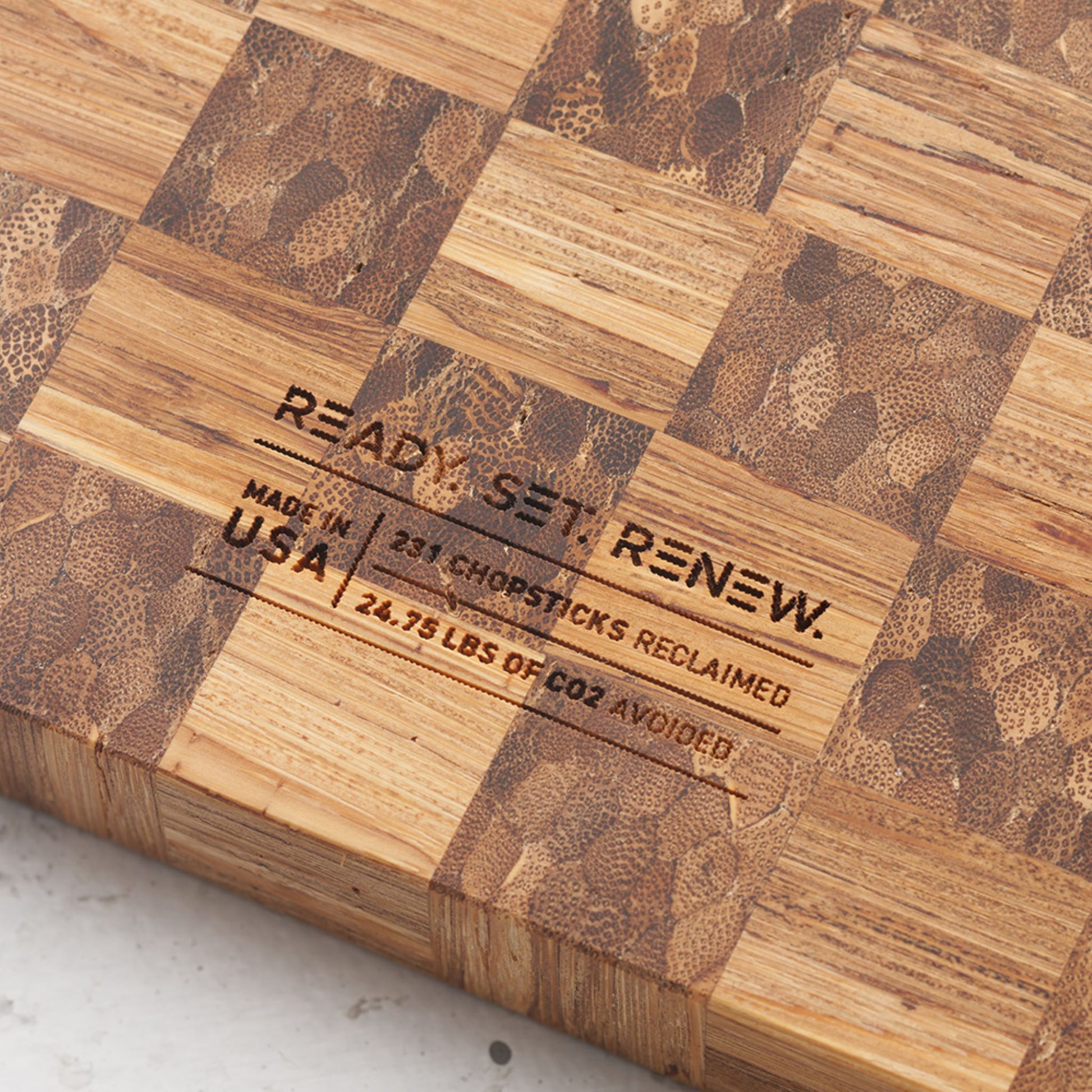 Close up view of the stamp on the back of the board that reads renew made in the usa two hundred and thirty one chopsticks reclaimed and twenty four point seventy five pounds of co2 avoided