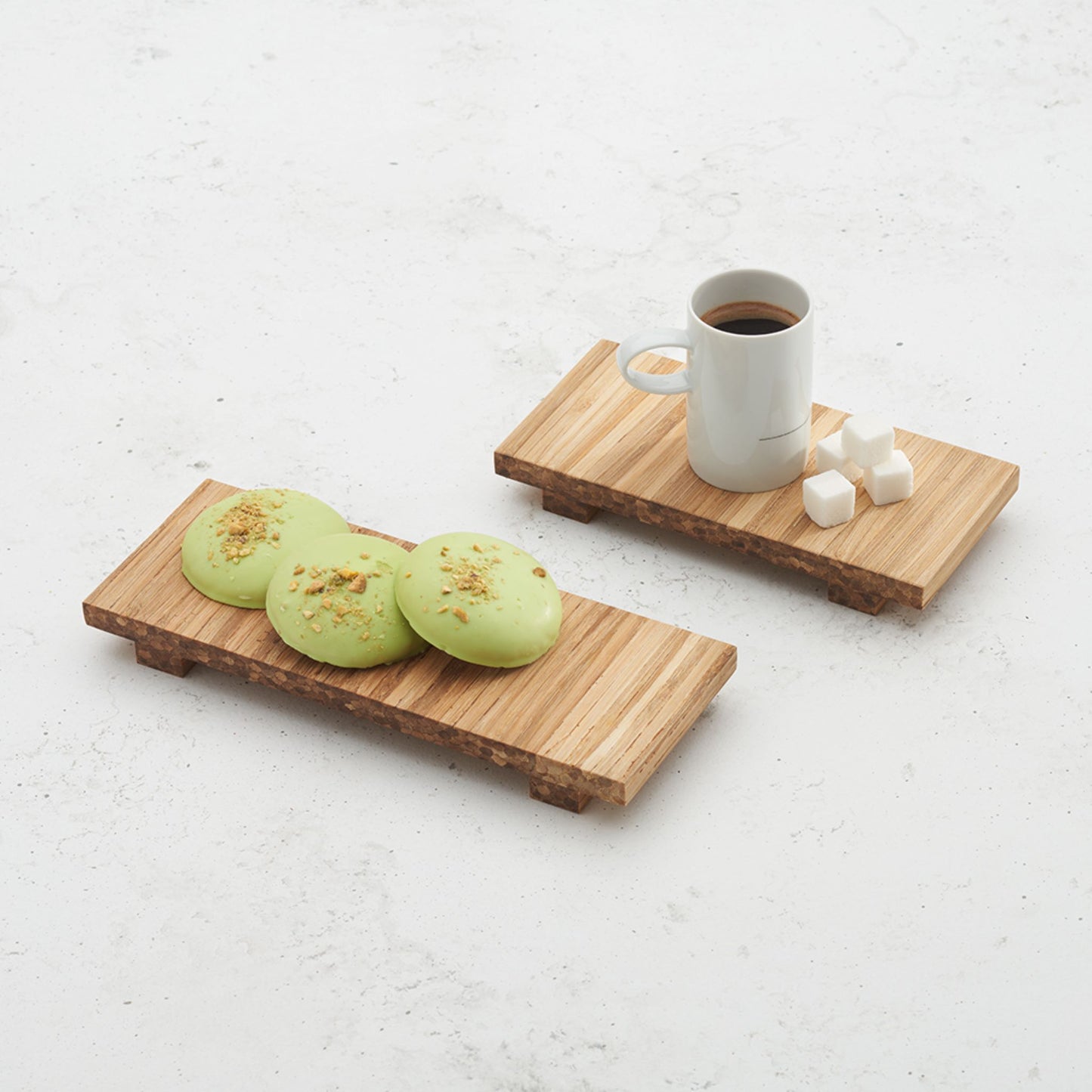 Two heyday breakfast trays sitting on a counter top. One with a coffee mug and sugar cubes on top, another with three mini cakes on top