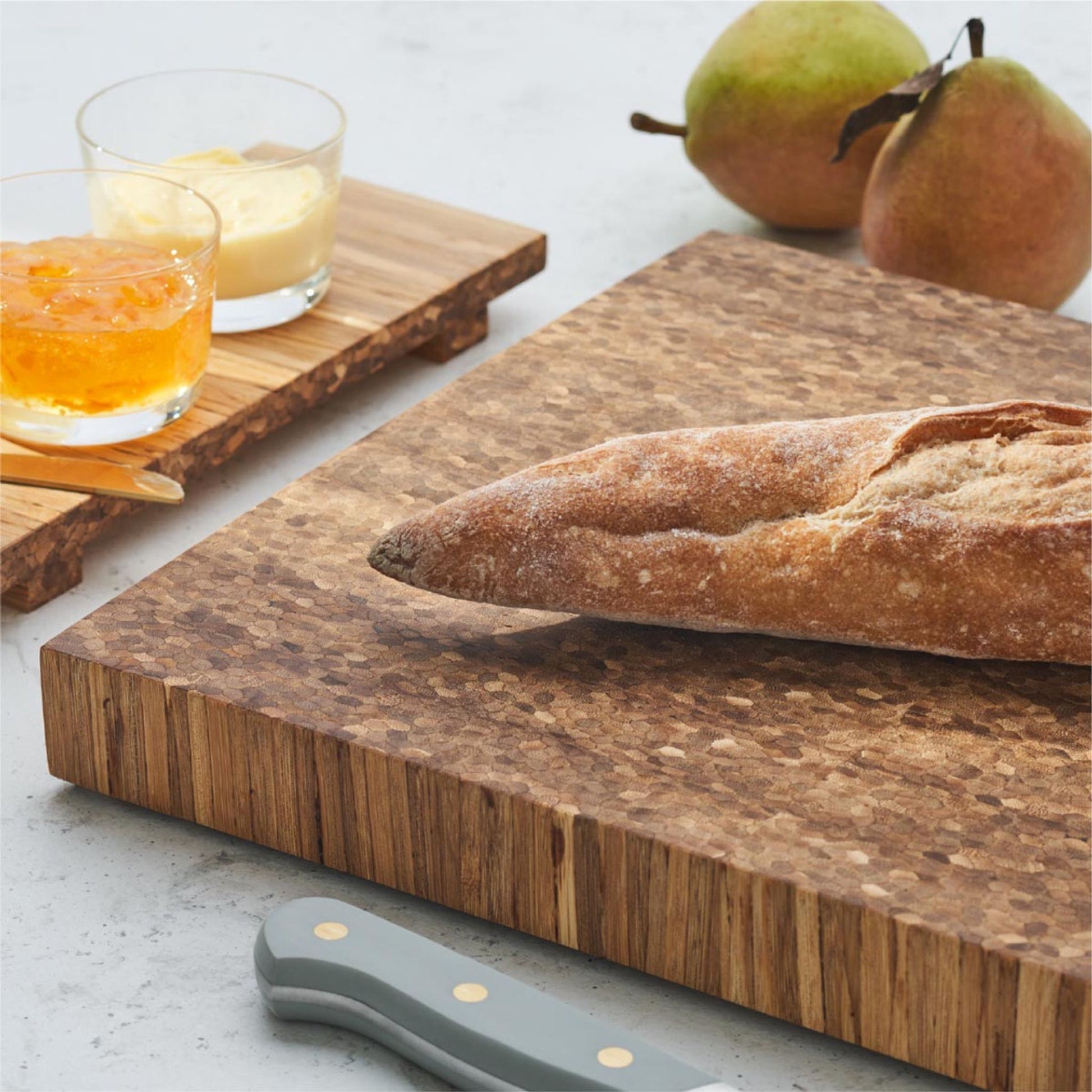 bread on top of bread board, surrounded by a tray with 2 cups of sauce and 2 pears