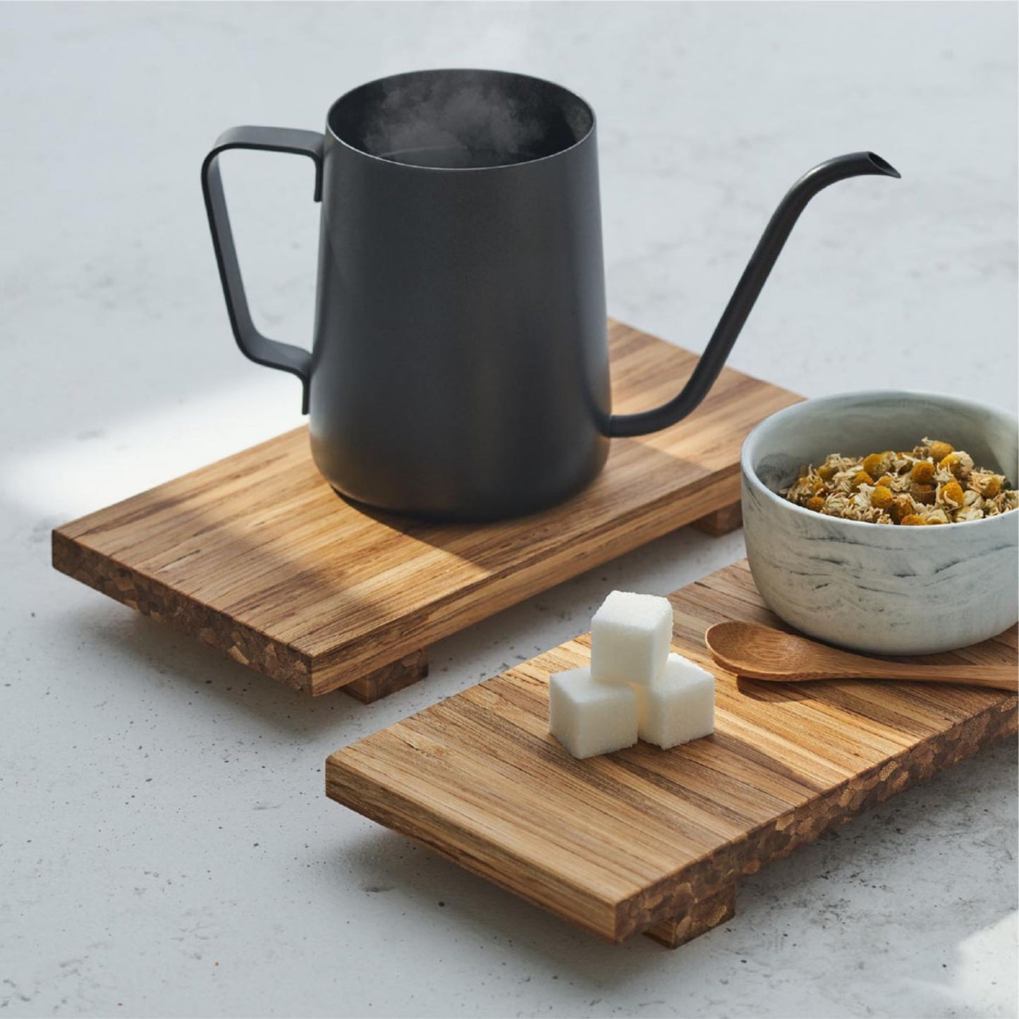 a tea pot on one tray, a bowl and three sugar cubes on another tray