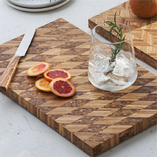 A cup of iced water, four slices of orange, and a knife on the multi grain bread board