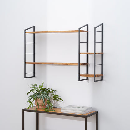 A modern, wall-mounted shelving unit features two long, rectangular wood shelves held by dark metal frames on the left, and a smaller, three-tiered unit with similar construction on the right. Below the shelves, a coordinating console table holds a terracotta potted plant and a stack of books against a white wall.