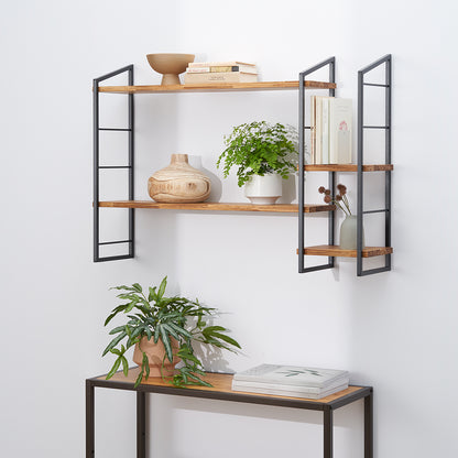 A pair of industrial-style, wall-mounted shelves featuring wood planks supported by black metal frames. The shelves are decorated with books, various potted plants, and wooden and ceramic vases, with a matching console table and plant below.