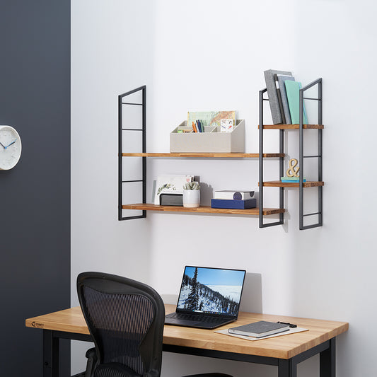 Wall-mounted shelving units, featuring two wood shelves supported by black metal frames, are installed above a light wood desk in a modern home office. The shelves hold various office supplies, books, and decorative items, with a laptop and notebook visible on the desk below.