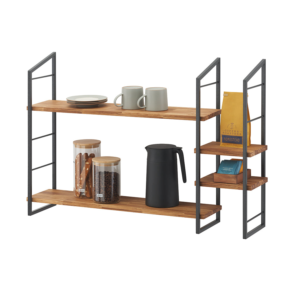Two-tiered kitchen or coffee bar shelving unit with a dark metal frame and warm wooden shelves, styled with various coffee accessories. The left side holds plates, mugs, a carafe, and glass jars with coffee beans and biscotti, while the right side features smaller shelves with a bag of coffee and tea packets.